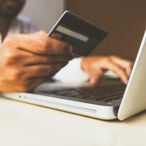 Mão segurando cartão de crédito em frente ao computador